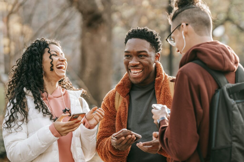 Three friends sharing a joyful moment, laughing together outdoors in a park setting.